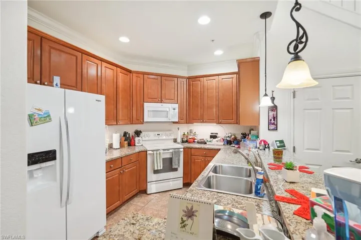 Kitchen with white appliances, brown cabinetry, a sink, and pendant lighting