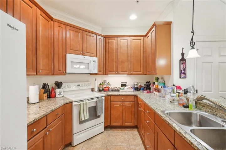 Kitchen with white appliances, brown cabinetry, a sink, and light tile patterned flooring