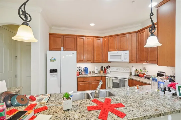 Kitchen featuring ornamental molding, white appliances, pendant lighting, and a sink