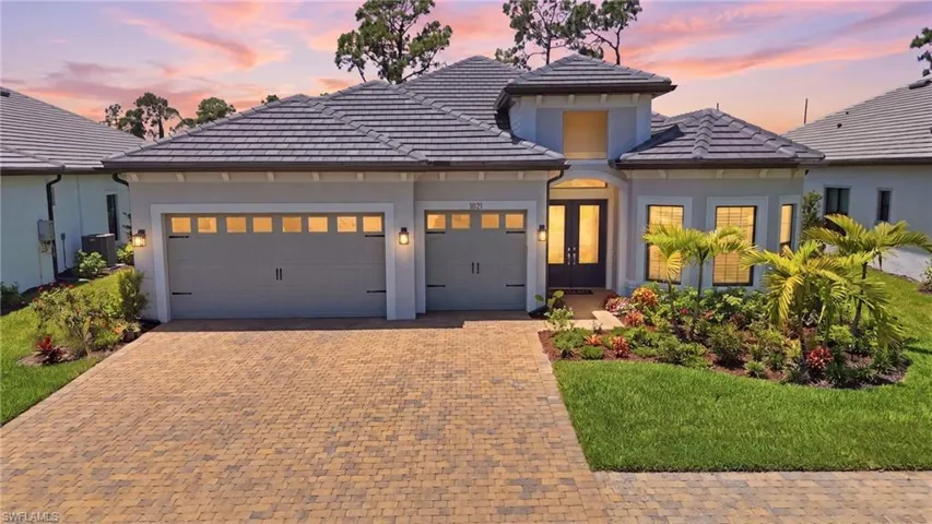 Modern stucco exterior with a tile roof, featuring a paver driveway, an inviting entry with double doors, and a meticulously landscaped front yard