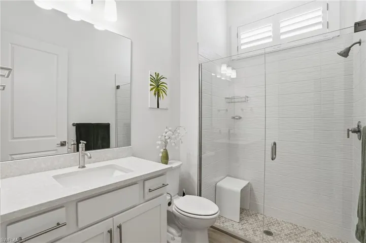 Bathroom featuring a single vanity with stone-finish countertop and undermount sink, a large frameless mirror, and a glass-enclosed shower