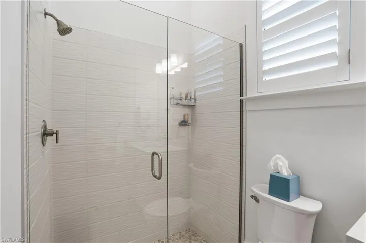 Glass-enclosed shower featuring a mosaic tile floor, horizontal textured wall tile, and brushed nickel fixtures