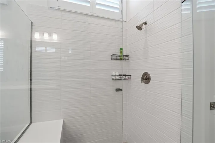 Shower with textured white tile walls, brushed nickel fixtures, glass enclosure, and an integrated bench