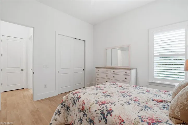 Bright interior featuring wood-finish flooring, a window with white louvered shutters, and a closet with bifold doors