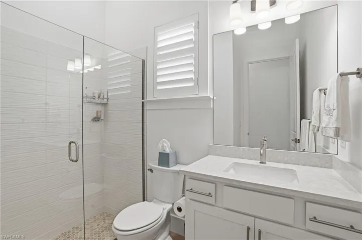 Contemporary bathroom featuring a glass-enclosed shower with textured tile, a single vanity with a solid surface countertop, an undermount sink, and a brushed nickel faucet