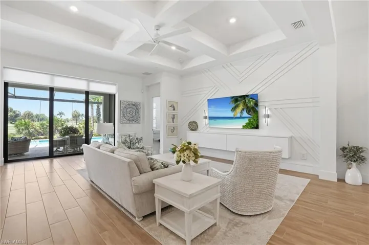 Expansive living area featuring coffered ceilings, wood-finish flooring, and a decorative accent wall