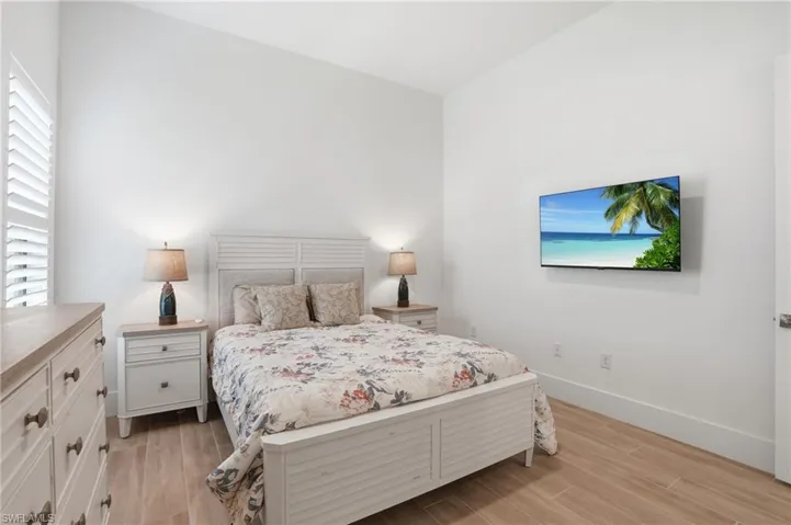 Bedroom featuring wood-finish flooring, plantation shutters, and a wall-mounted television