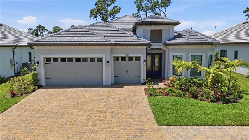 Contemporary stucco exterior with a tiled hip roof, featuring a paver driveway, two-car garage, and lush landscaping