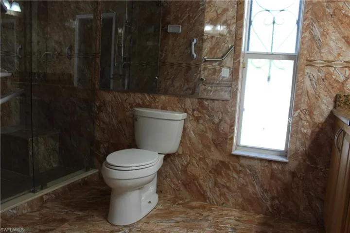 Bathroom featuring tile floors, an enclosed shower, toilet, and tile walls