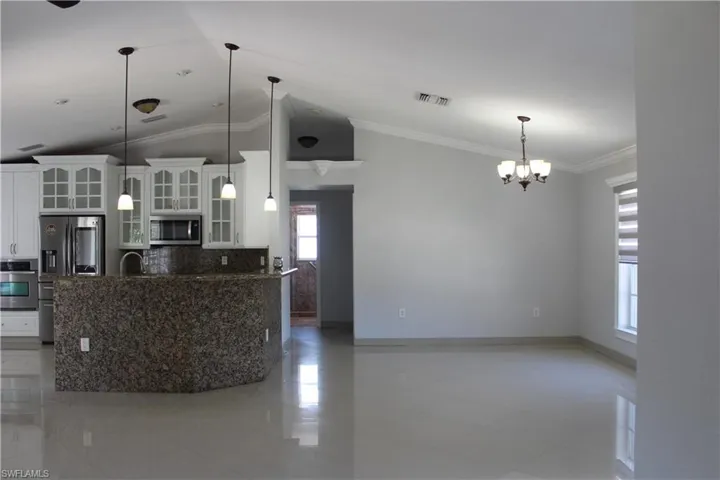 Kitchen featuring tile flooring, crown molding, pendant lighting, white cabinetry, and appliances with stainless steel finishes