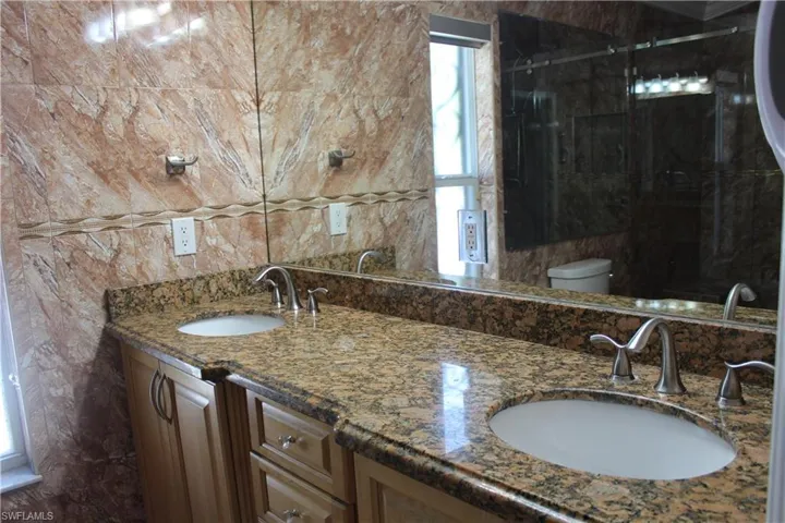 Bathroom with tile walls, oversized vanity, toilet, and double sink