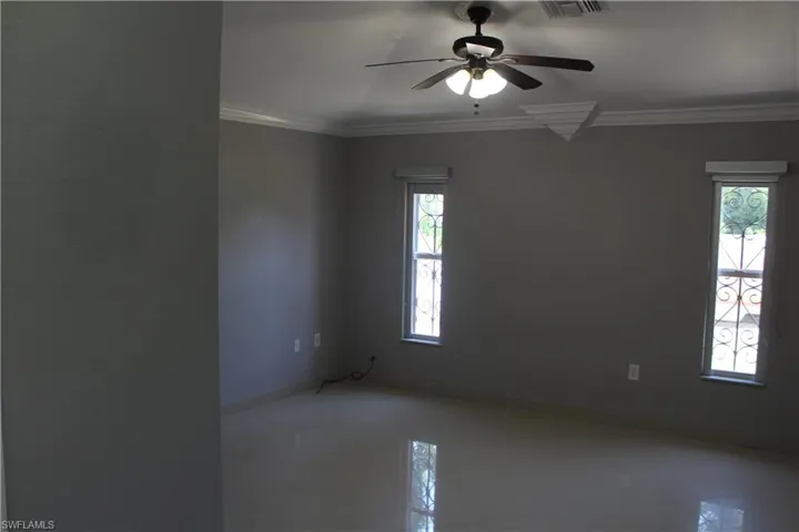 Tiled empty room with ceiling fan and crown molding