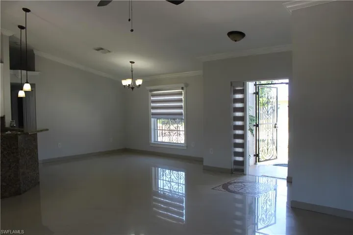 Tiled empty room with ornamental molding and ceiling fan with notable chandelier