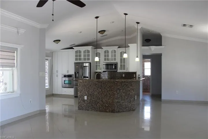 Kitchen with ceiling fan, vaulted ceiling, light tile flooring, white cabinets, and appliances with stainless steel finishes