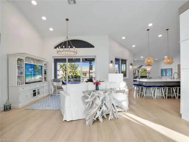 Living room with high vaulted ceiling, sink, light wood-type flooring, and a notable chandelier