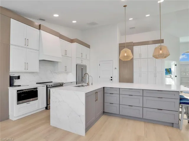 Kitchen with gray cabinets, appliances with stainless steel finishes, pendant lighting, sink, and custom exhaust hood
