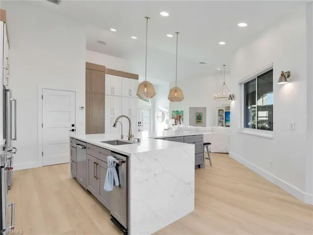 Kitchen with sink, light stone counters, hanging light fixtures, light wood-type flooring, and an island with sink