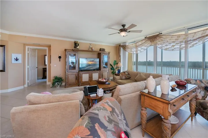 Living area with light tile patterned flooring, ornamental molding, and ceiling fan