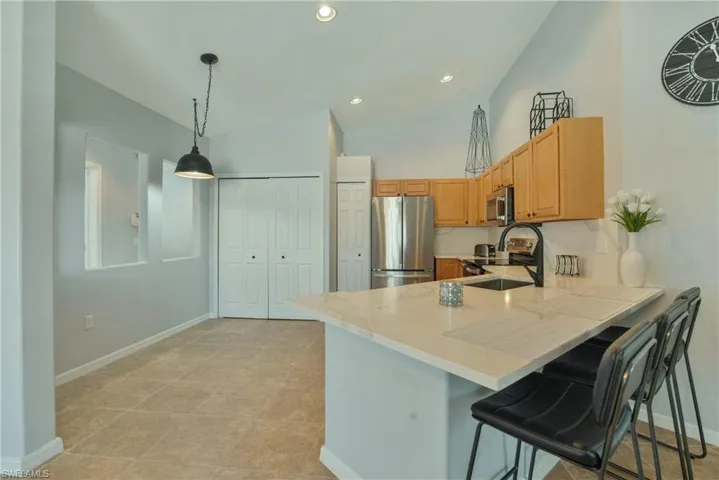 Kitchen with light countertops, stainless steel appliances, a breakfast bar, pendant lighting, and vaulted ceiling