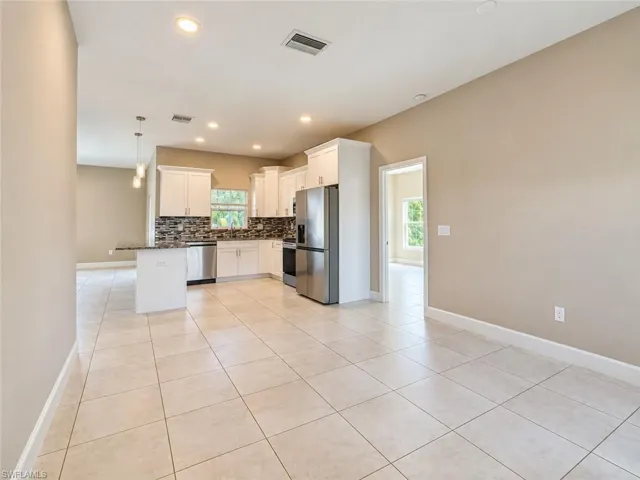 Kitchen featuring white shaker cabinetry, stainless steel appliances, a multi-tone tile backsplash, and a breakfast bar with pendant lighting