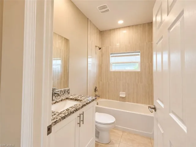 Bathroom featuring a white vanity with a speckled countertop, a drop-in sink, a built-in bathtub, and tiled walls