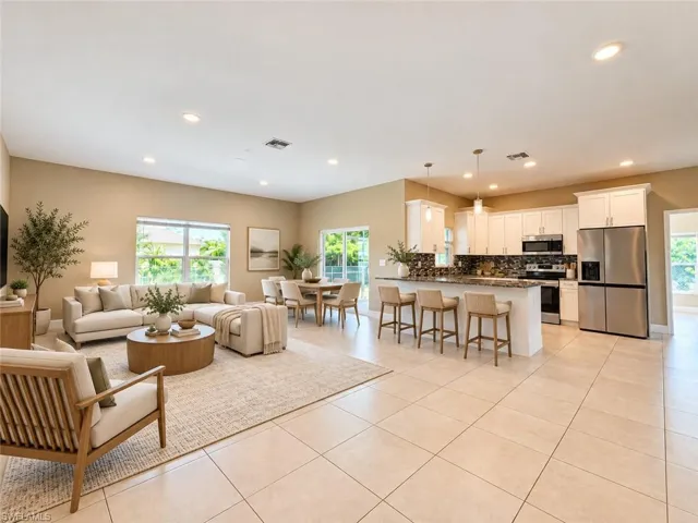 Spacious open-concept living area featuring large format tile flooring, recessed lighting, a kitchen with white cabinetry and stainless steel appliances, and a dining area with ample natural light