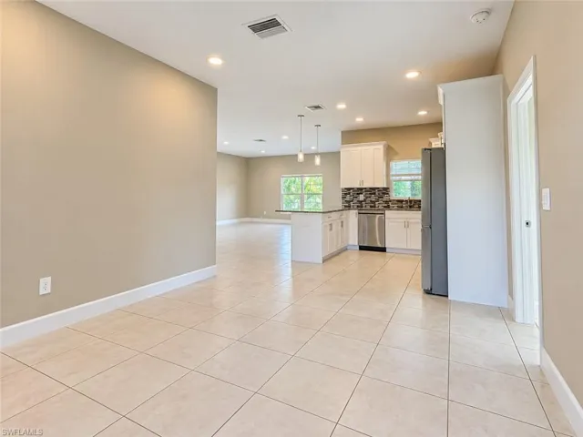 Open-concept kitchen and living area featuring tile flooring, recessed lighting, white cabinetry, stainless steel appliances, and a mosaic tile backsplash