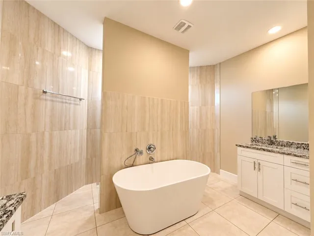 Freestanding soaking tub, tiled shower enclosure, dual vanity with granite countertop, large wall-mounted mirror, and recessed lighting