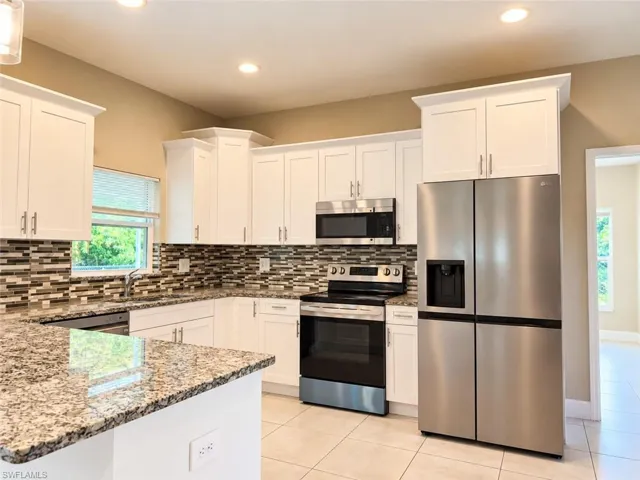 Kitchen featuring white shaker cabinetry, speckled countertops, mosaic tile backsplash, and stainless steel appliances