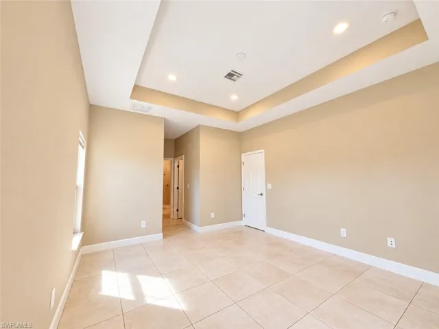 Tray ceiling with recessed lighting, tiled flooring, neutral wall tones, white trim, and a paneled interior door