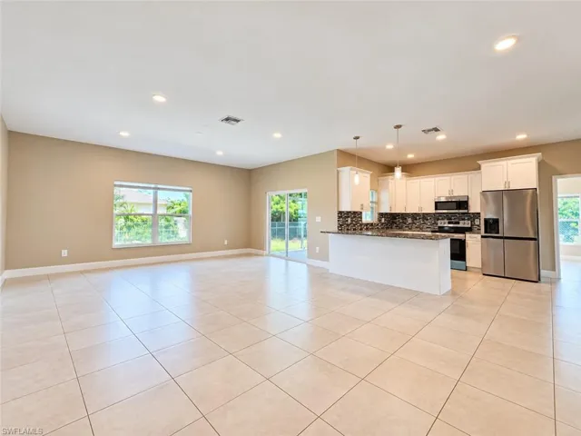 Open-concept living space with large format tile flooring, recessed lighting, and a white kitchen featuring stainless steel appliances and a breakfast bar with pendant lighting