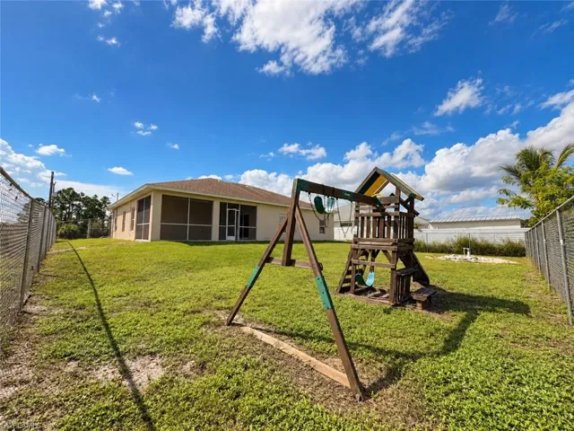 Expansive backyard featuring a chain-link fence, mature palm trees, and a screened patio