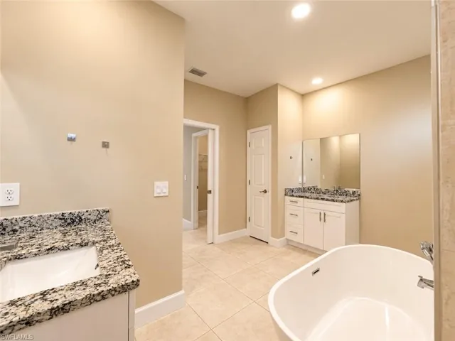 Dual vanity with granite countertops, tiled flooring, recessed lighting, and a freestanding soaking tub