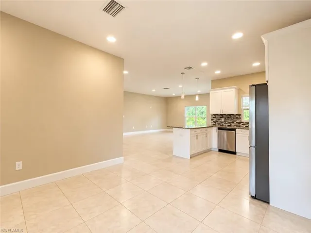 Open-concept living space with light-toned tile flooring, recessed lighting, and a kitchen island with pendant lighting