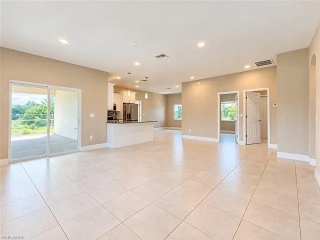 Spacious open-concept interior with recessed lighting, light-toned tile flooring, and sliding glass doors to the exterior