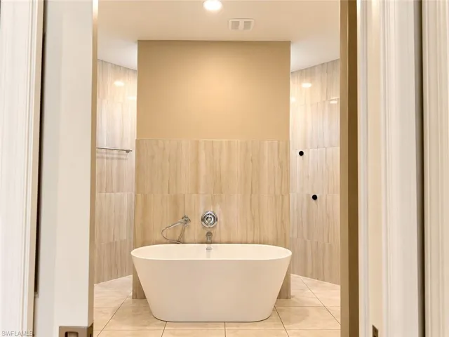 Freestanding soaking tub with chrome fixtures, set against floor-to-ceiling tiled walls