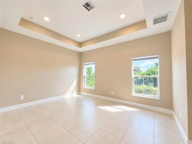 Recessed ceiling lighting, tray ceiling, two windows, tiled flooring, and neutral wall tones