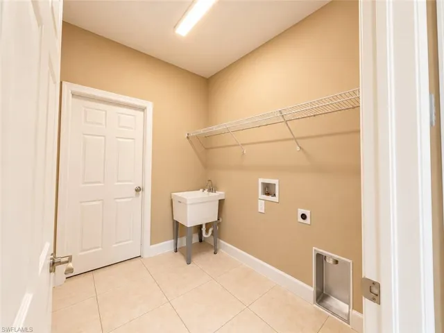 Utility room featuring ceramic tile flooring, a utility sink, wire shelving, and overhead lighting
