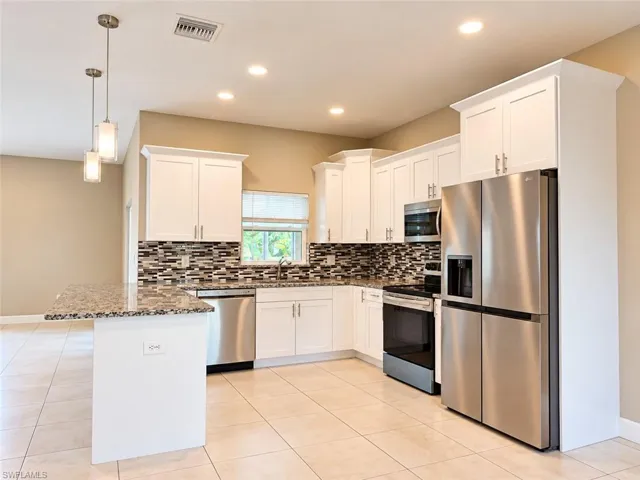 Contemporary kitchen featuring white cabinetry, stainless steel appliances, mosaic tile backsplash, and a breakfast bar with stone countertops