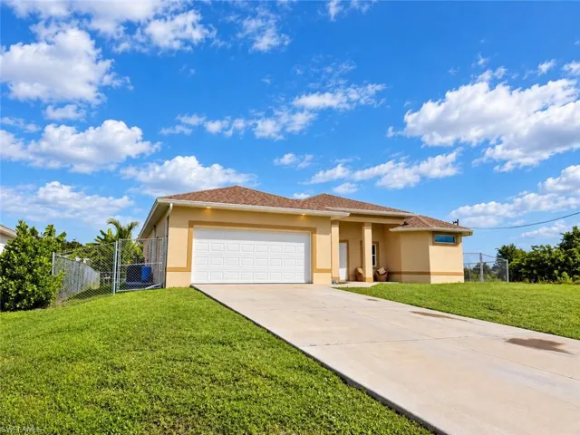 Stucco exterior with a shingle roof, attached garage, concrete driveway, and a chain-link fence