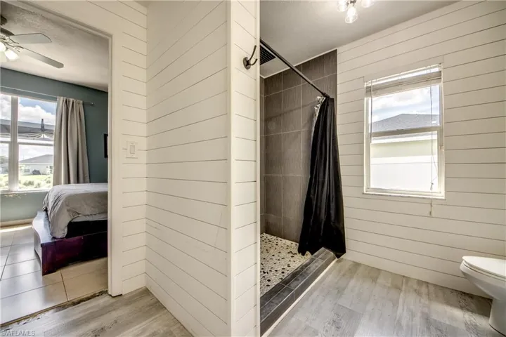Full bathroom with a shower stall, plenty of natural light, ensuite bath, light wood finished floors, and wooden walls