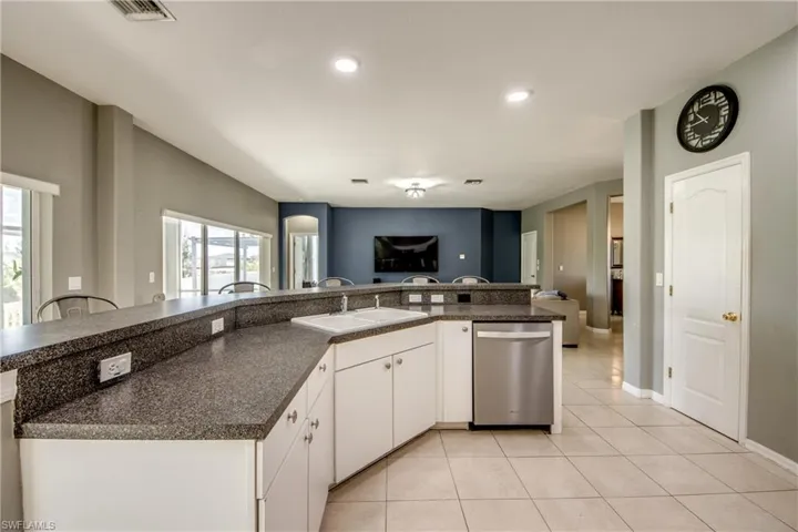Kitchen with white cabinetry, open floor plan, stainless steel dishwasher, light tile patterned floors, and an island with sink
