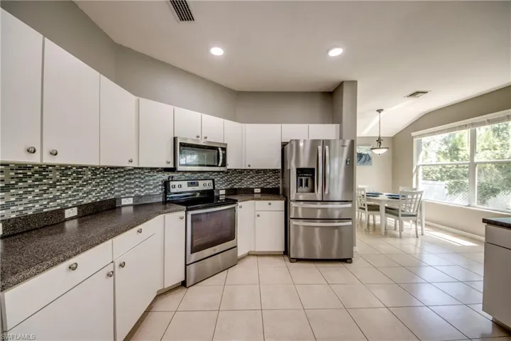 Kitchen featuring stainless steel appliances, white cabinets, pendant lighting, light tile patterned floors, and vaulted ceiling