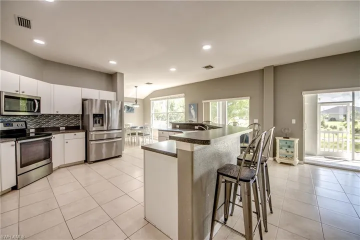 Kitchen featuring stainless steel appliances, dark countertops, a spacious island, light tile patterned flooring, and a breakfast bar area