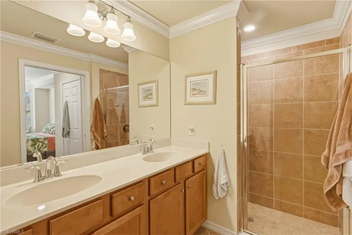 Bathroom featuring ornamental molding, double vanity, a shower stall, and ensuite bathroom
