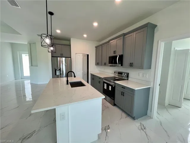 Kitchen with gray cabinets, sink, an island with sink, stainless steel appliances, and light stone countertops