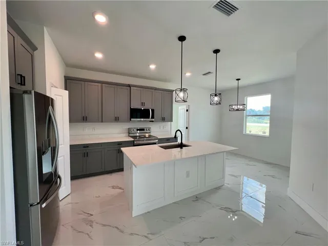 Kitchen featuring pendant lighting, an island with sink, sink, gray cabinets, and appliances with stainless steel finishes