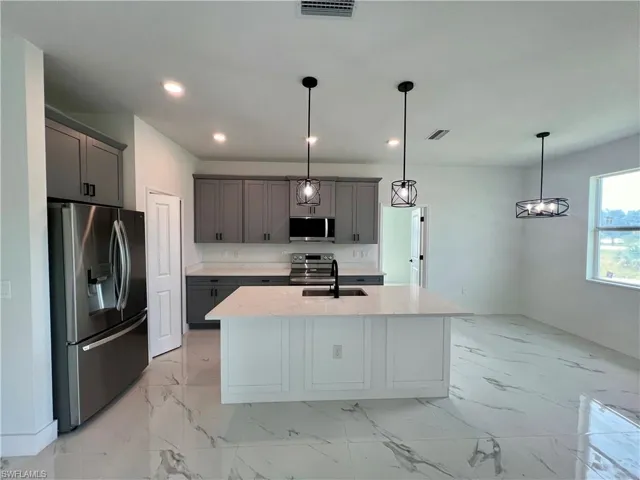 Kitchen featuring gray cabinetry, an island with sink, pendant lighting, stainless steel appliances, and sink