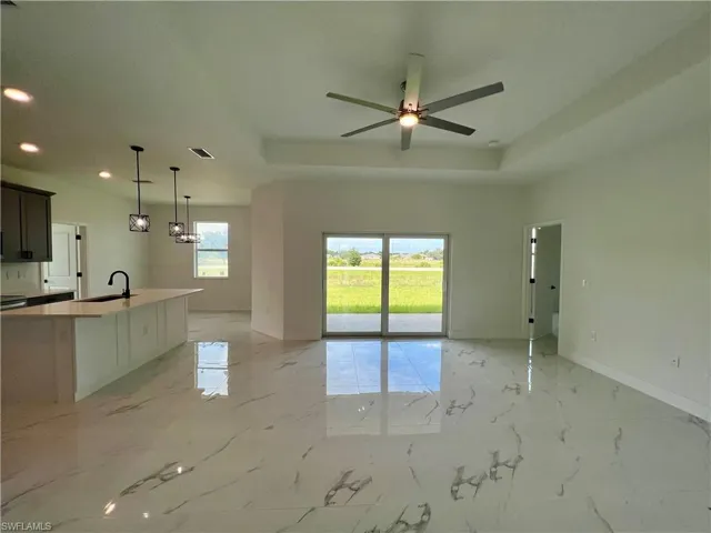 Living room featuring a raised tray ceiling, sink, ceiling fan, and plenty of natural light