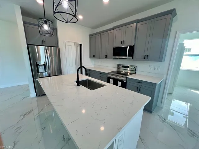 Kitchen featuring appliances with stainless steel finishes, light QUARTZ counters, decorative light fixtures, a kitchen island with sink, and sink